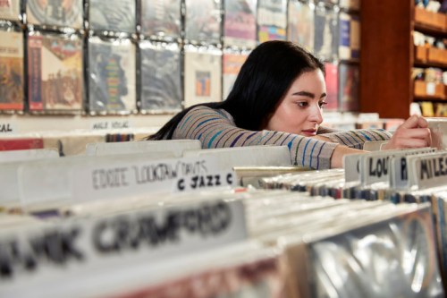 A young woman browses through vinyl records in a music store, focused on finding a specific album.