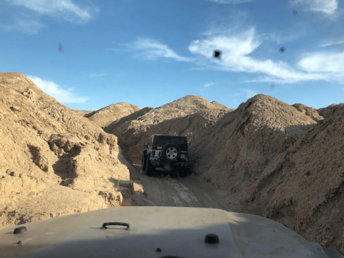 A rugged off-road trail with two vehicles navigating through sandy hills under a clear blue sky.