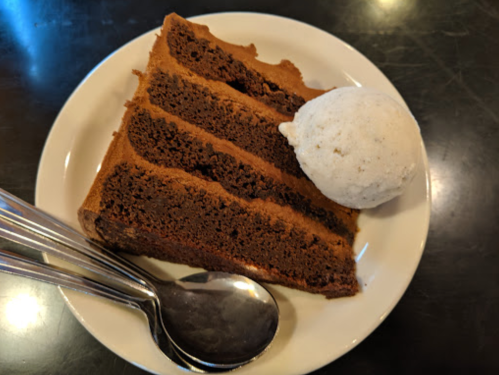 A slice of chocolate cake with three layers, served with a scoop of vanilla ice cream on a white plate.