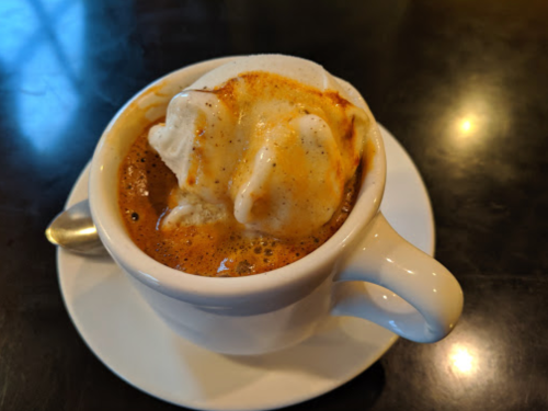 A cup of espresso topped with a scoop of creamy vanilla ice cream, served on a white saucer.