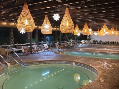 Cozy pool area with woven pendant lights, surrounded by lounge chairs and palm trees, creating a relaxing atmosphere.