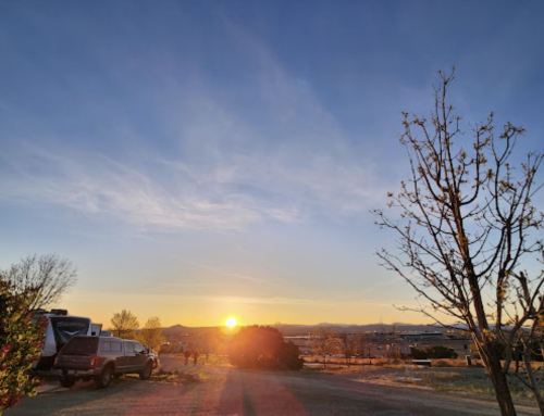 A sunset over a landscape with trees and vehicles, casting warm light across the scene.