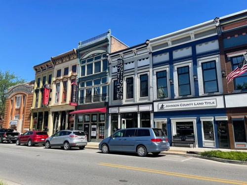 A row of colorful storefronts along a street, featuring a boutique and a land title office, with parked cars in front.