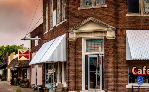 Historic brick building with a bank sign, awnings, and nearby cafes on a small-town street.