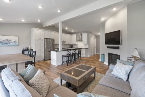 Modern open-concept living area with a kitchen, dining table, and cozy seating, featuring light colors and wooden floors.