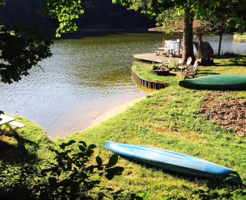 A serene lakeside scene with a blue kayak, grassy shore, and wooden dock surrounded by trees.