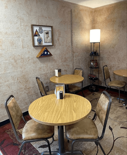 Cozy café interior with two wooden tables, chairs, and a decorative wall featuring framed items and a lamp.