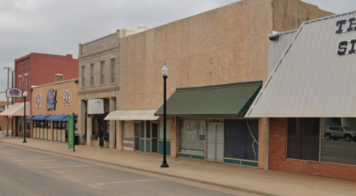 A quiet street scene featuring several storefronts with awnings and a cloudy sky overhead.