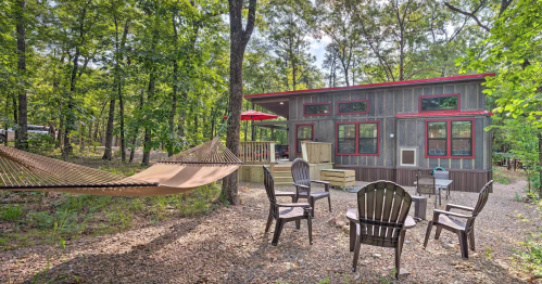 Cozy cabin in a wooded area with a hammock, outdoor seating, and a porch surrounded by trees.
