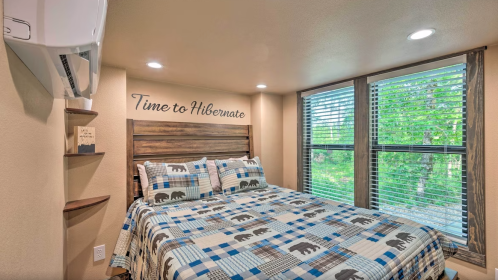Cozy bedroom with a wooden bed, bear-themed bedding, and large windows overlooking greenery. "Time to Hibernate" on the wall.