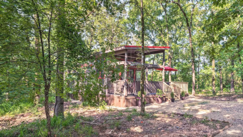 A modern cabin nestled in a lush green forest, featuring a deck and red roof, surrounded by trees.