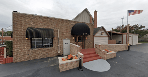 A brick building with an awning, steps, and pumpkins, featuring an American flag in the background.