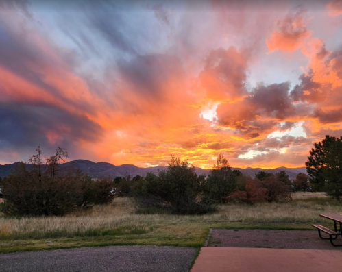 A vibrant sunset with orange and purple clouds over a grassy landscape and distant mountains.