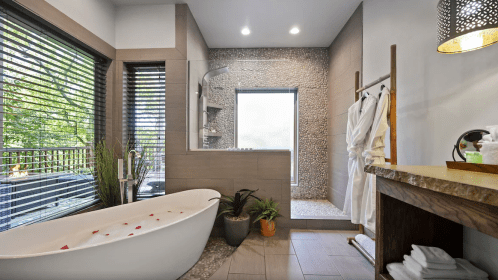 A modern bathroom featuring a freestanding tub, glass shower, and natural decor with plants and soft lighting.
