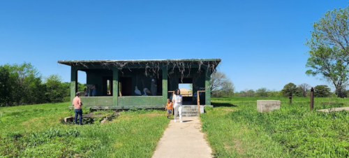 A green building surrounded by grass, with people walking on a path in a clear blue sky.
