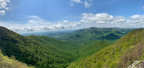 A panoramic view of lush green mountains under a blue sky with scattered clouds.