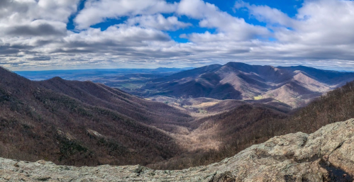 A panoramic view of rolling mountains under a cloudy sky, with valleys and trees in the foreground.
