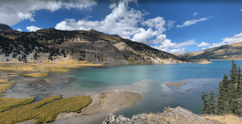 Scenic view of a lake surrounded by mountains and trees under a partly cloudy sky.