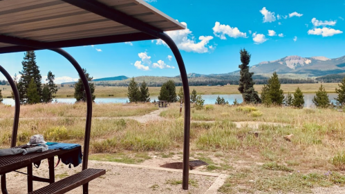 A scenic view of a lake surrounded by mountains and trees, with a picnic area in the foreground under a shelter.