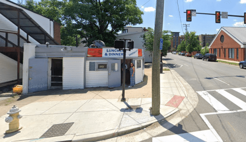 A small diner with a sign reading "Lunch & Dinner" on a street corner, with traffic lights and a crosswalk nearby.