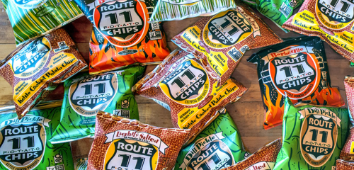 A colorful assortment of Route 11 potato chip bags in various flavors scattered on a wooden surface.