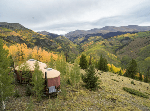 A scenic view of mountains and valleys with autumn foliage, featuring two round structures in the foreground.