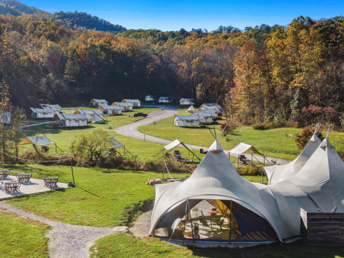 Aerial view of a glamping site with tents and a winding path, surrounded by colorful autumn trees.