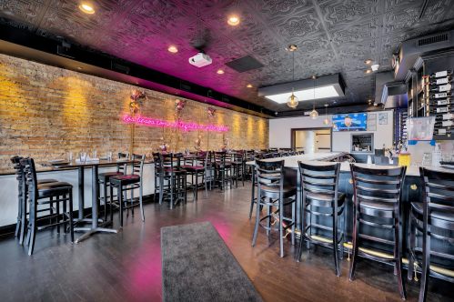 Interior of a modern restaurant featuring brick walls, neon lights, and dark wooden tables and chairs.