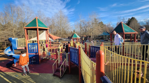 A colorful playground with slides and climbing structures, surrounded by trees and a clear blue sky.