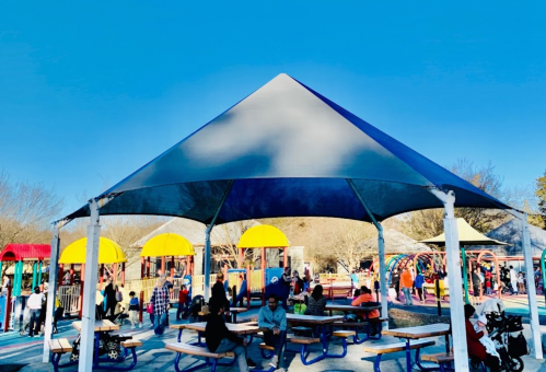 A shaded playground area with colorful structures and families enjoying the space on a sunny day.