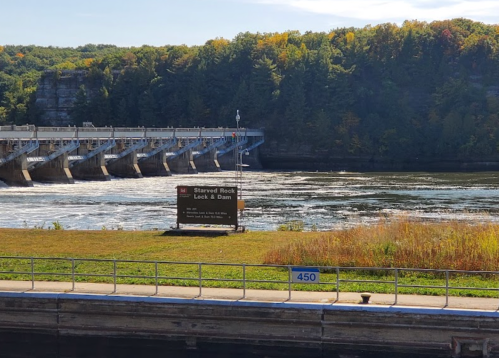 View of Starved Rock Lock and Dam with a river and lush green trees in the background on a sunny day.