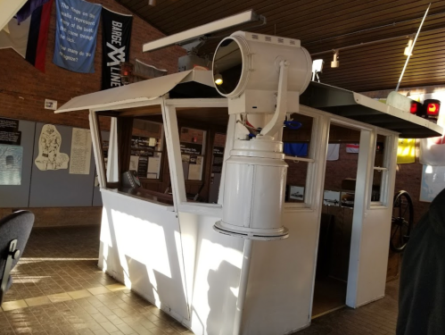 A vintage boat cabin interior with a large circular window and various nautical equipment displayed.