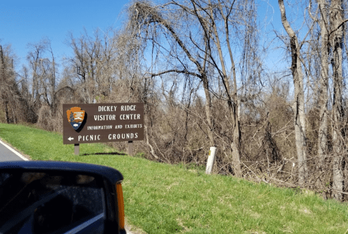 Sign for Dickey Ridge Visitor Center with directions to picnic grounds, surrounded by bare trees and blue sky.