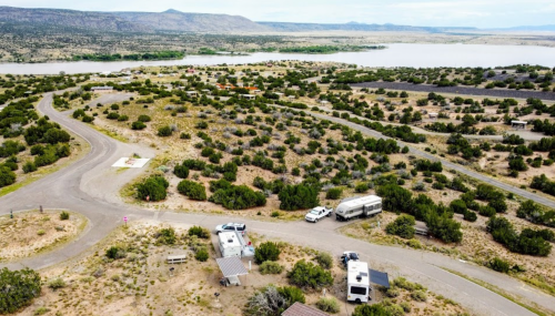 Aerial view of a winding road through a green landscape with RVs parked near a lake and mountains in the background.