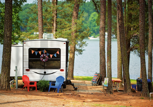 A cozy RV by a lake, surrounded by trees, with colorful chairs and festive decorations.
