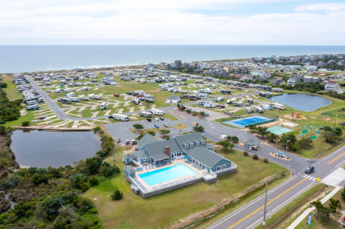 Aerial view of a coastal campground with RVs, a pool, playground, and nearby ponds, overlooking the ocean.