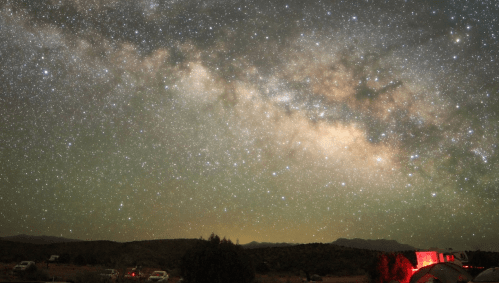 A stunning night sky filled with stars and the Milky Way, with silhouettes of mountains and trees in the foreground.