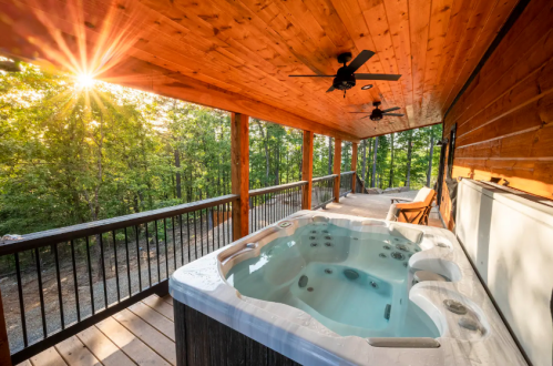 A hot tub on a wooden deck surrounded by trees, with sunlight streaming through the leaves.