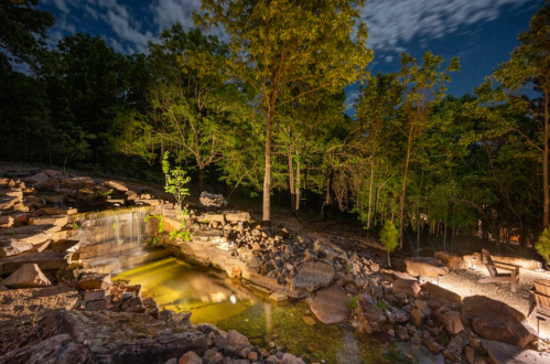 A serene nighttime scene of a rocky waterfall surrounded by trees, with soft lighting illuminating the area.