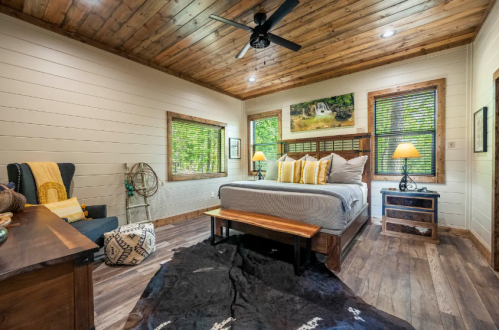 Cozy bedroom with wooden ceiling, a large bed, decorative pillows, and warm lighting from bedside lamps.