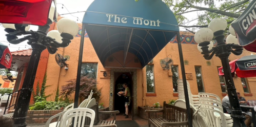 Entrance of The Mont restaurant with outdoor seating and colorful decor, surrounded by trees and patio lights.