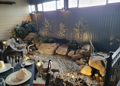 A cozy dining area featuring a small indoor stream with rocks and plants, illuminated by soft lights.