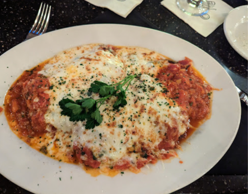 A plate of cheesy baked pasta topped with herbs and a rich tomato sauce, served on a black tablecloth.