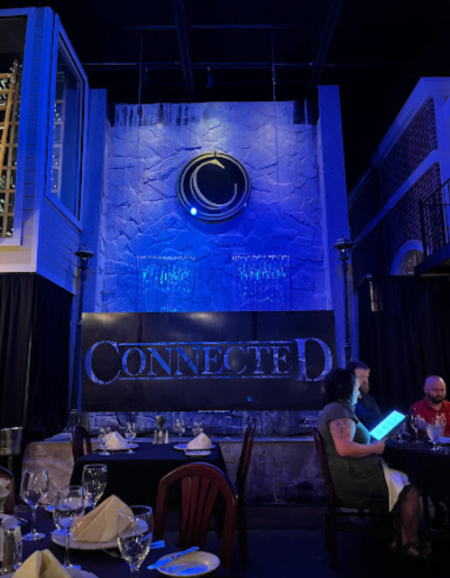 A dimly lit restaurant interior featuring a water wall, blue lighting, and tables set for dining.