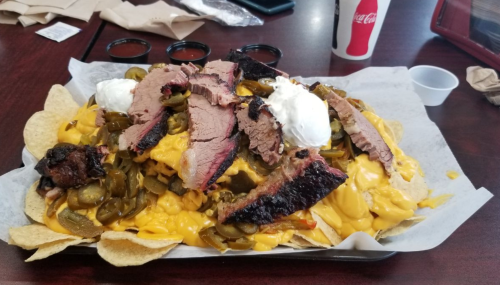 A large plate of nachos topped with cheese, jalapeños, brisket, and dollops of sour cream.