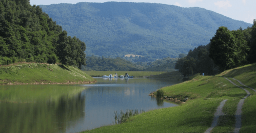 A serene landscape featuring a calm river, lush green banks, and distant mountains under a clear blue sky.