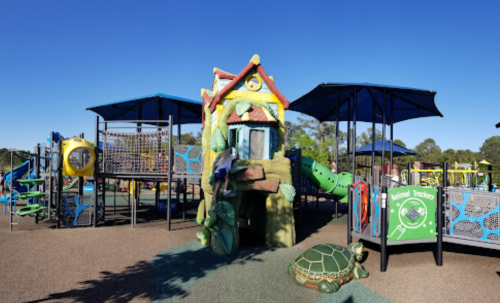 Colorful playground with a treehouse structure, slides, climbing features, and a turtle sculpture on the ground.