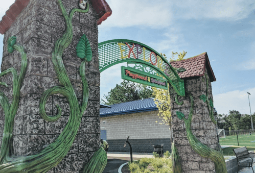 Colorful entrance archway to a playground, featuring vines and the word "EXPLORE" against a blue sky.
