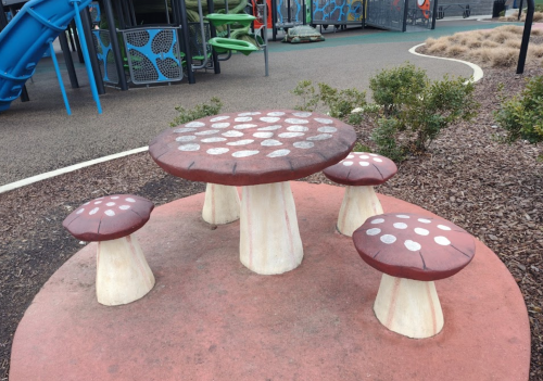 A whimsical mushroom-shaped table with four matching stools in a playground setting.