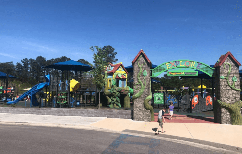 Colorful playground entrance with slides, climbing structures, and a sign reading "EXPLORE" under a clear blue sky.